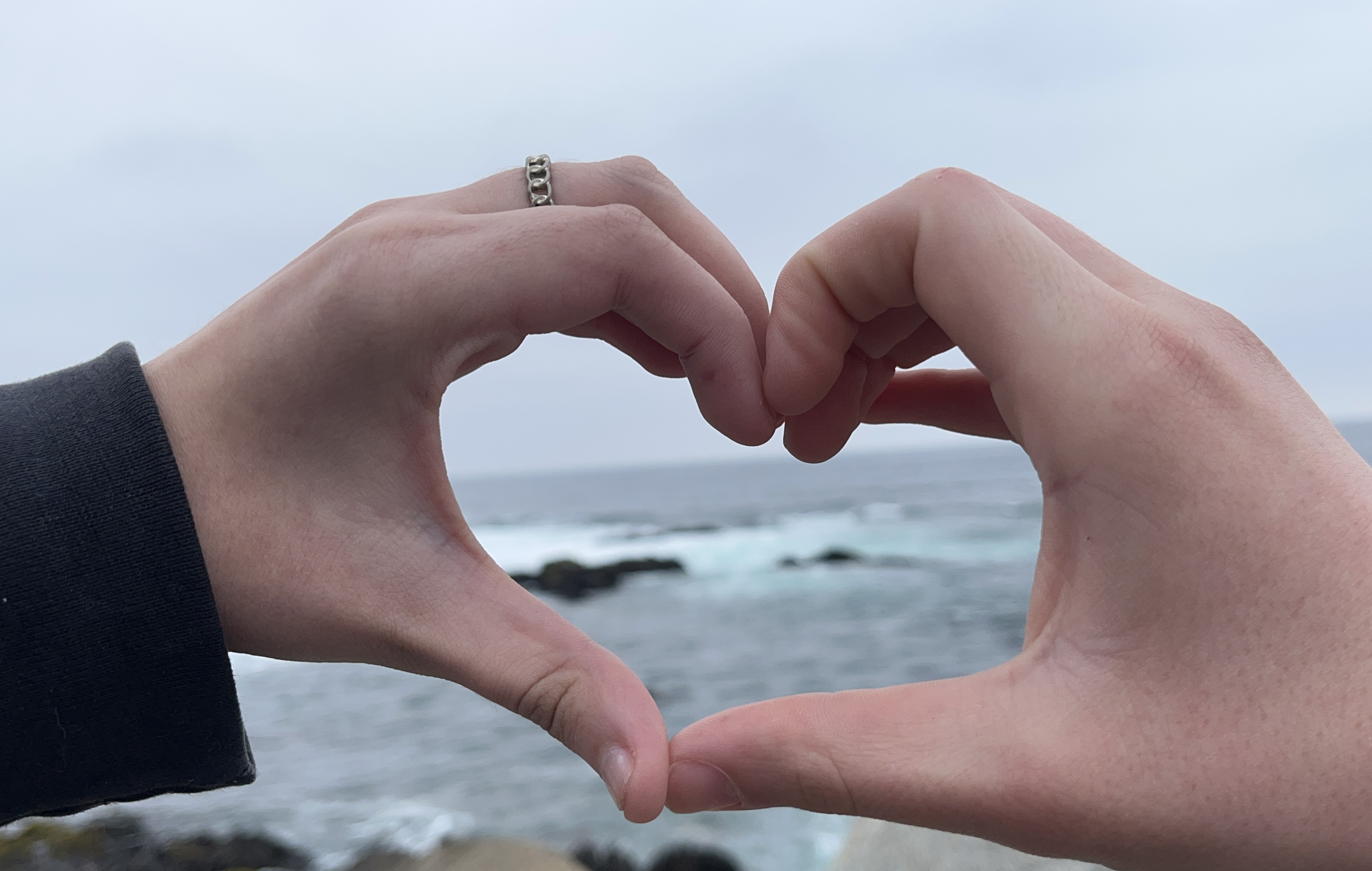 Sus manos formando un corazón frente al mar